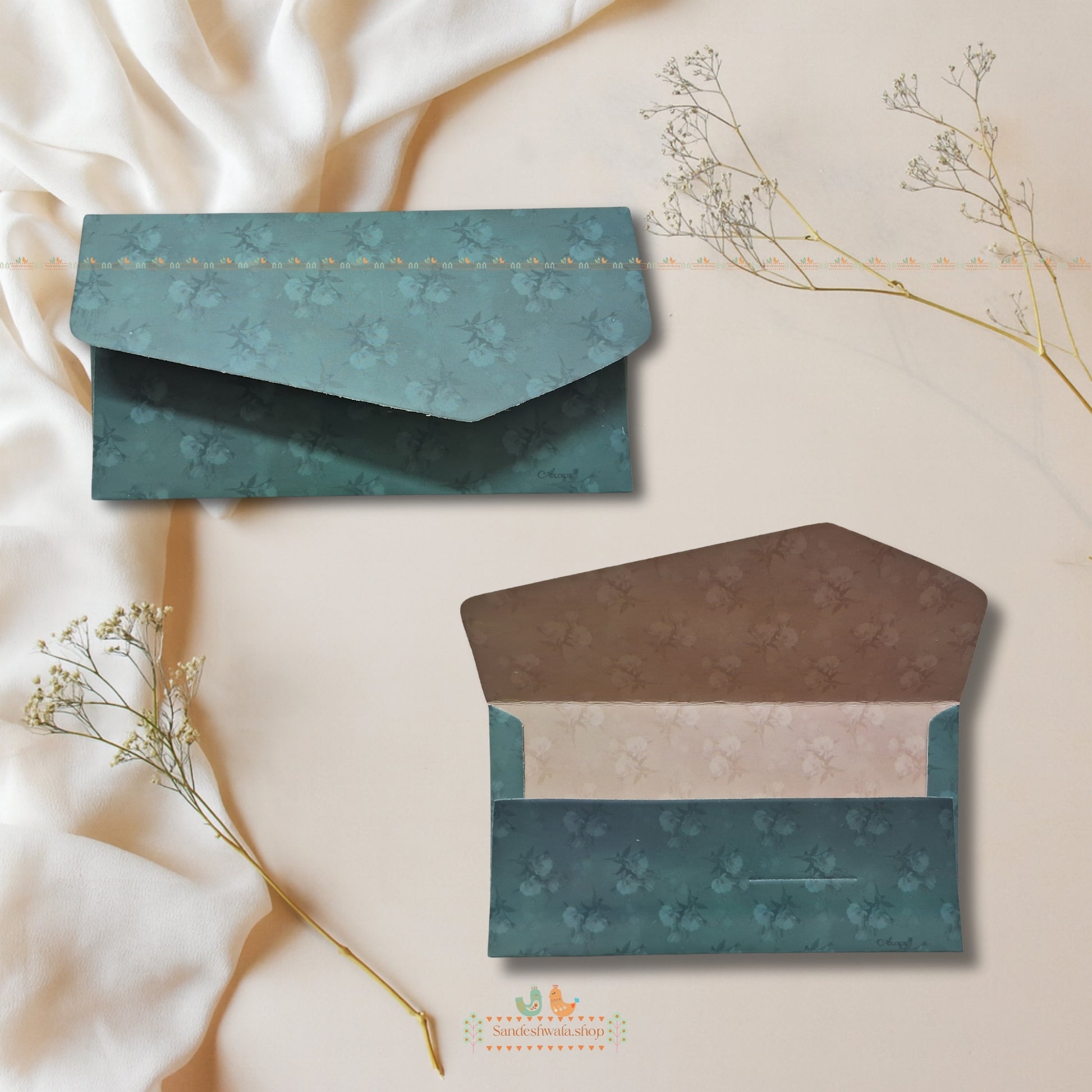 Two patterned envelopes on a beige fabric background with dried flowers.